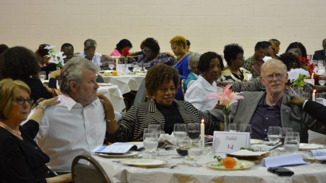 The image shows Jews and African Americans touching each others shoulders, in blessing, at a seder table. 